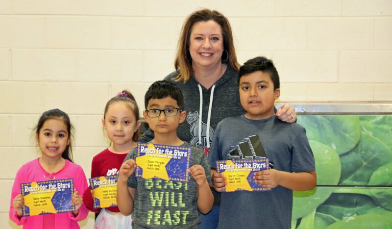 Mrs. Clarke smiles with her students receiving awards.