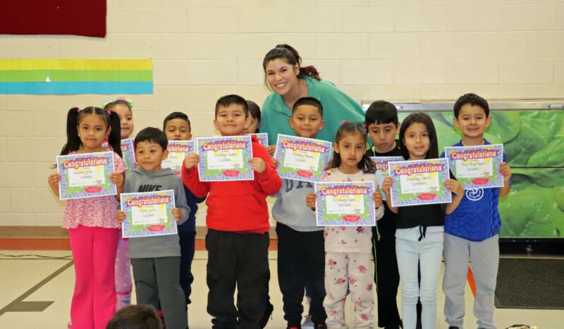 Ms. Resendiz smiles with her students receiving awards.